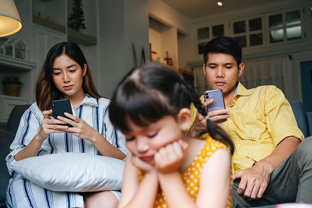 parents ignoring their young child to look at their phones